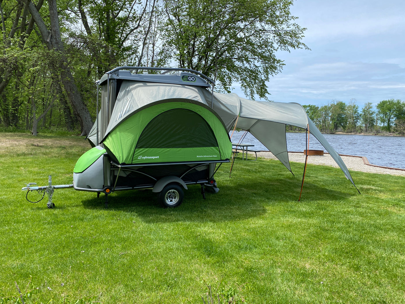 A SylvanSport Go compact camper trailer, perfect for an rv rental, is set up by the lake for outdoor adventures. — photo 8