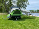 A SylvanSport Go compact camper trailer, perfect for an rv rental, is set up by the lake for outdoor adventures.