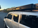Silver vehicle with black Roofnest rooftop tent. Ideal for RV rental trips or camping adventures. Low sun reflections on glass.