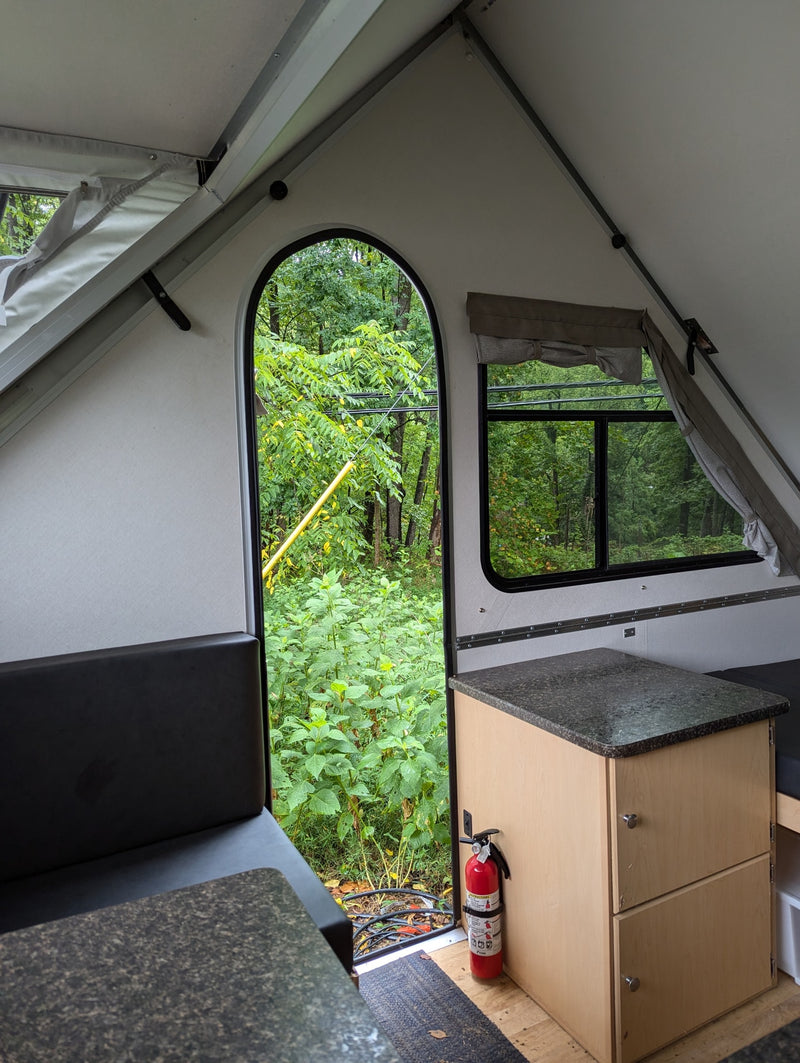 Cozy A-frame rv rental interior showcasing a forest view, compact kitchen, and fire safety. — photo 8