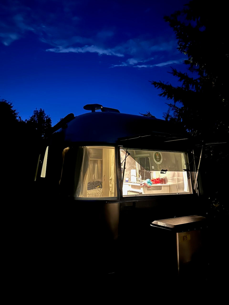Experience a night in an Airstream rv rental. Cozy interior lights reveal a full kitchen, glowing at dusk.