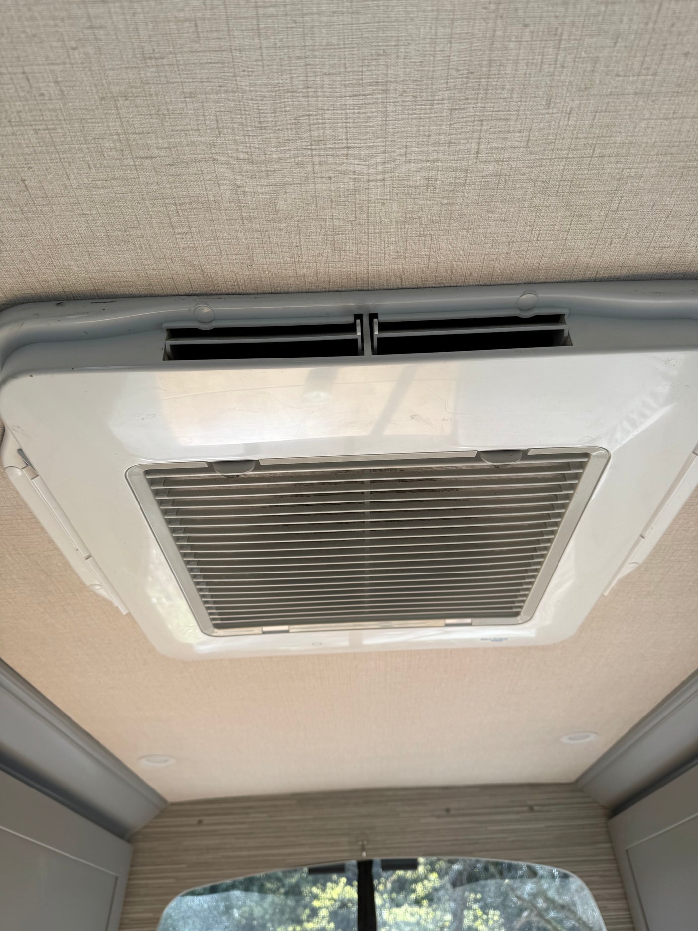 Overhead view of an rv rental's ceiling, featuring a white air conditioner unit with vents. The light-colored ceiling has a textured finish.