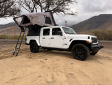 White Jeep Gladiator rv rental with rooftop tent on sand, perfect for camping and outdoor adventures.