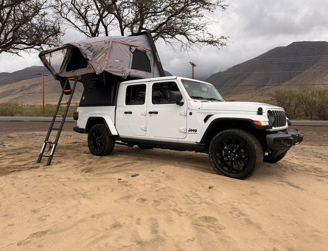 White Jeep Gladiator rv rental with rooftop tent on sand, perfect for camping and outdoor adventures.
