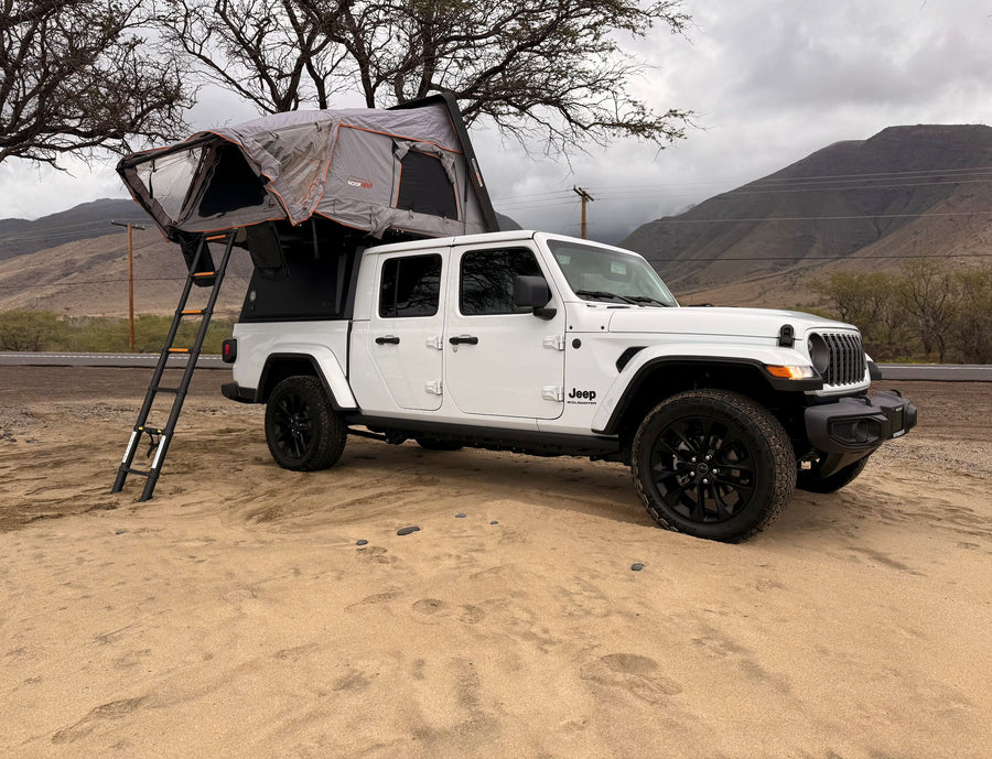 White Jeep Gladiator rv rental with rooftop tent on sand, perfect for camping and outdoor adventures.