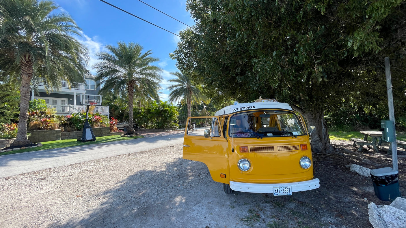 Experience vintage charm! This yellow Westfalia camper van, perfect for an RV rental, is parked on a sunny day near palm trees and a house.