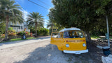 Experience vintage charm! This yellow Westfalia camper van, perfect for an RV rental, is parked on a sunny day near palm trees and a house.