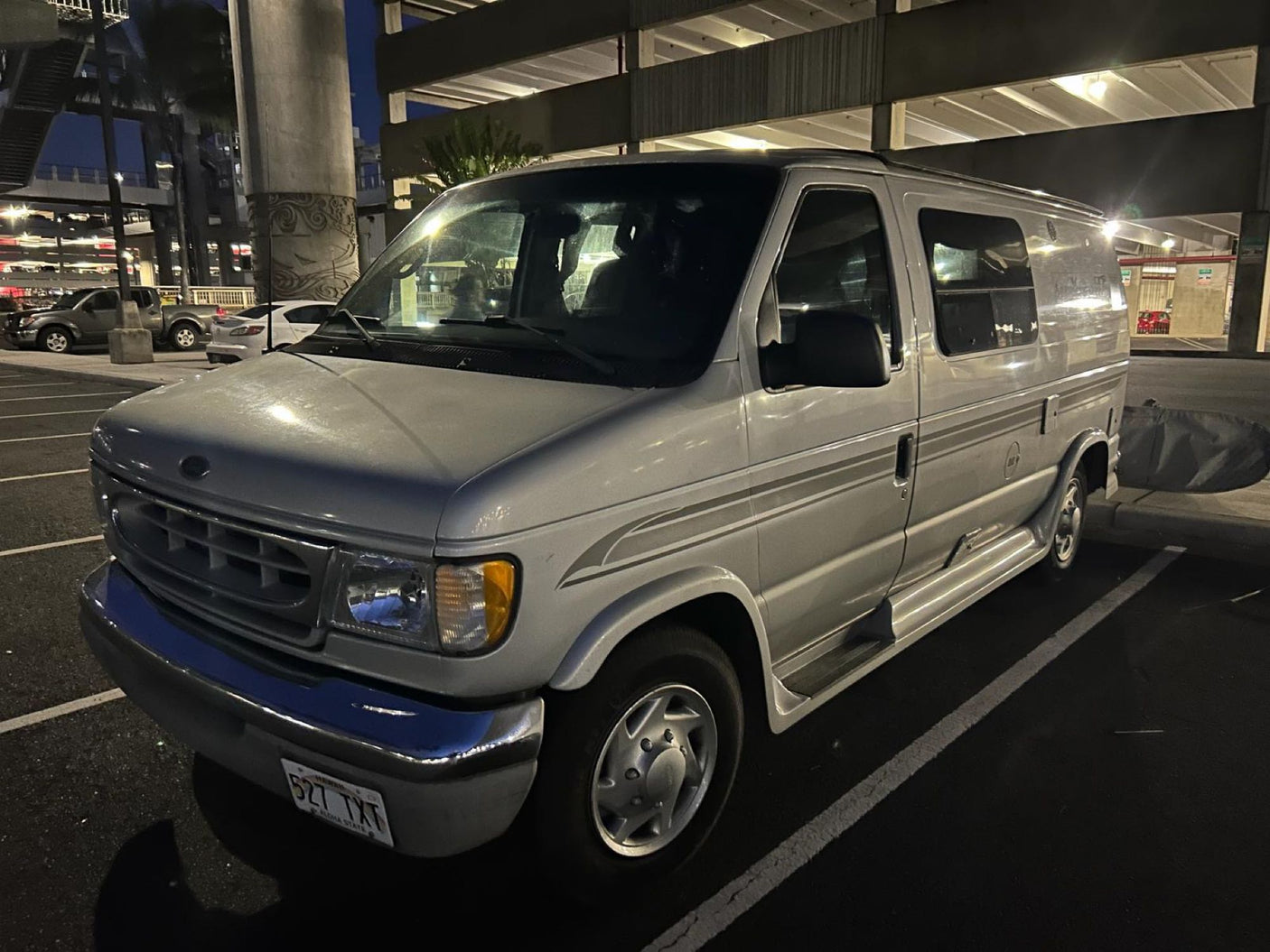 A silver Ford Econoline conversion van, ideal for an RV rental, parked at night. Great for exploring destinations.