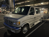 A silver Ford Econoline conversion van, ideal for an RV rental, parked at night. Great for exploring destinations.