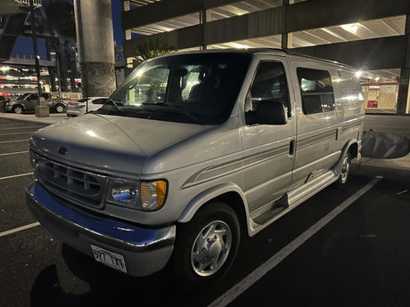 A silver Ford Econoline conversion van, ideal for an RV rental, parked at night. Great for exploring destinations.