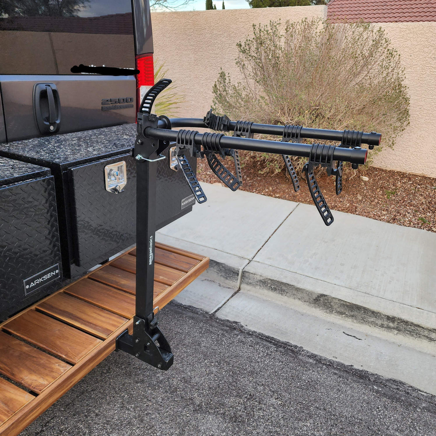 Tail of an RV rental van equipped with a multi-bike rack, ARKSEN storage boxes, and a wooden rear deck.