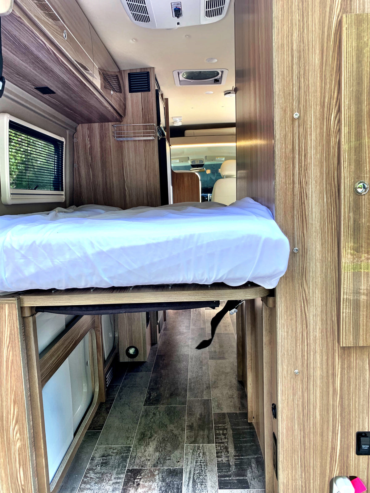 This RV rental offers a practical interior with a raised bed, wood walls, and a clear aisle leading to the front cabin. — photo 9