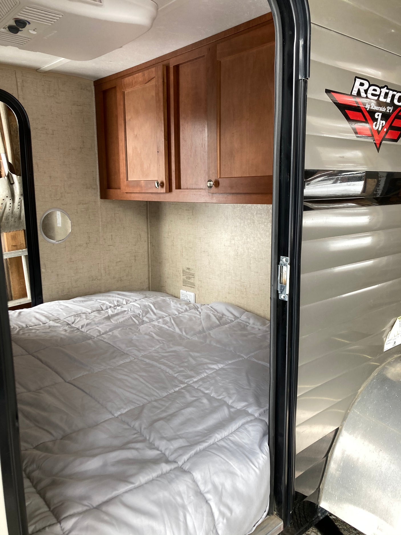 An RV rental's compact sleeping area featuring a neatly made bed, wooden cabinets, and ceiling AC.