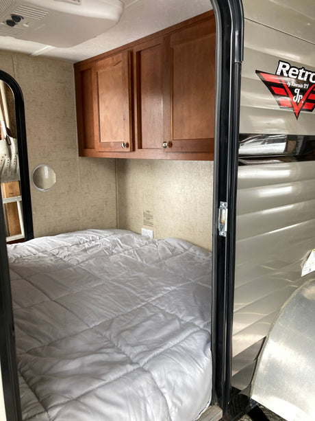 An RV rental's compact sleeping area featuring a neatly made bed, wooden cabinets, and ceiling AC.