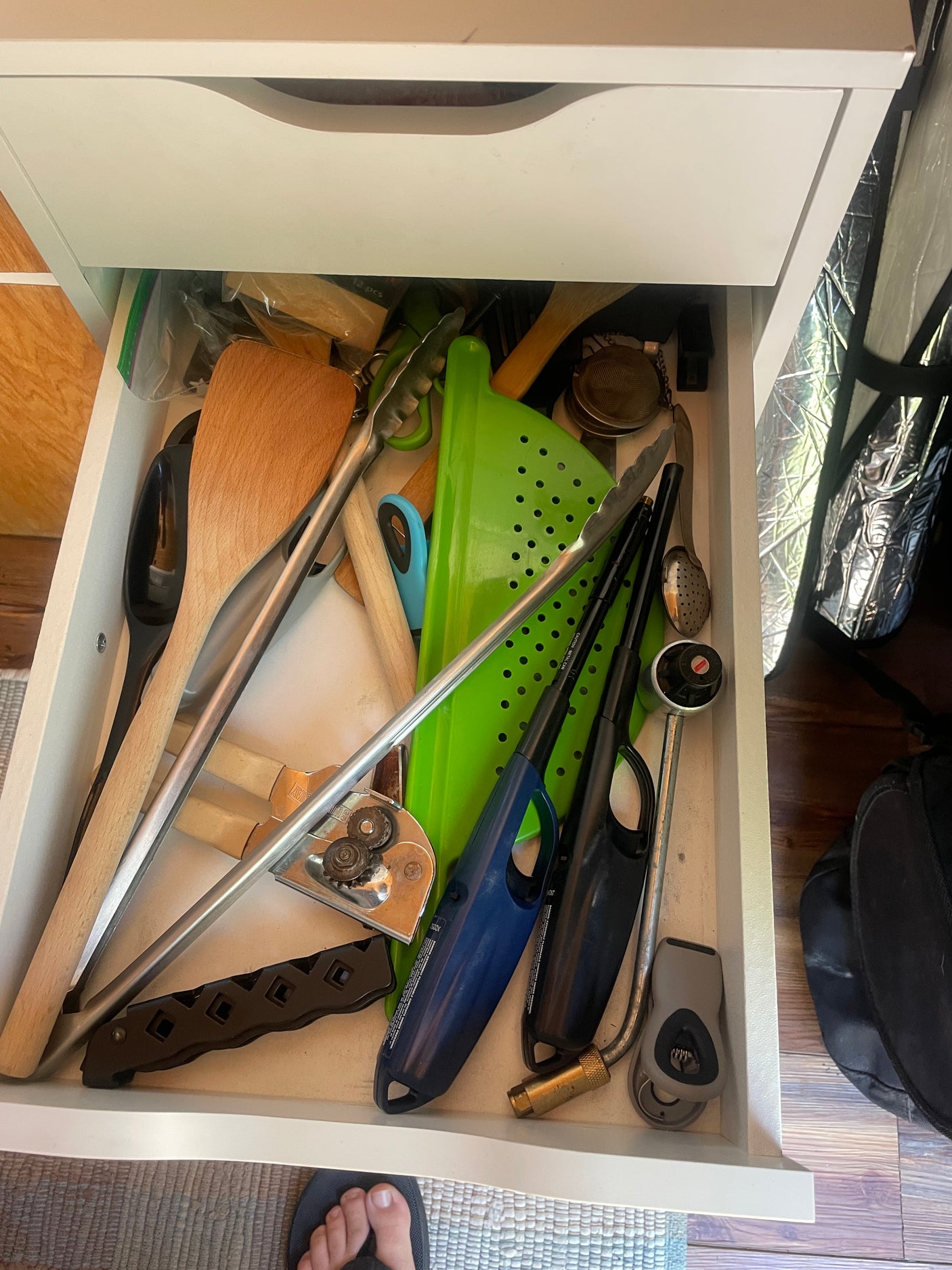 RV rental kitchen drawer: spatulas, tongs, lighters, colander, and other cooking essentials for travel.