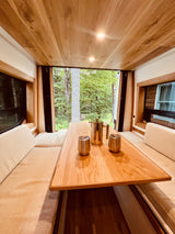 Cozy RV rental dining area with a forest view. Features a wooden table, bench seating, and a French press for coffee lovers.