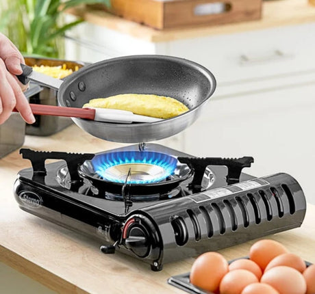 A person uses a portable gas stove to cook an omelet in a pan. Fresh eggs are nearby, perfect for an RV rental kitchen.
