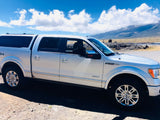 Silver F-150 pickup with camper shell, parked by mountains. Explore with this RV rental alternative under blue skies.