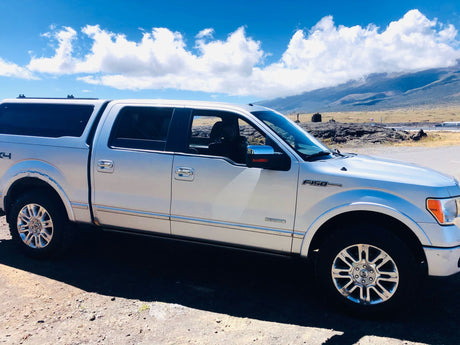 Silver F-150 pickup with camper shell, parked by mountains. Explore with this RV rental alternative under blue skies.