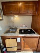 Inside an RV rental: a practical kitchen setup with a sink, two-burner stove, and ample storage in wood cabinets.