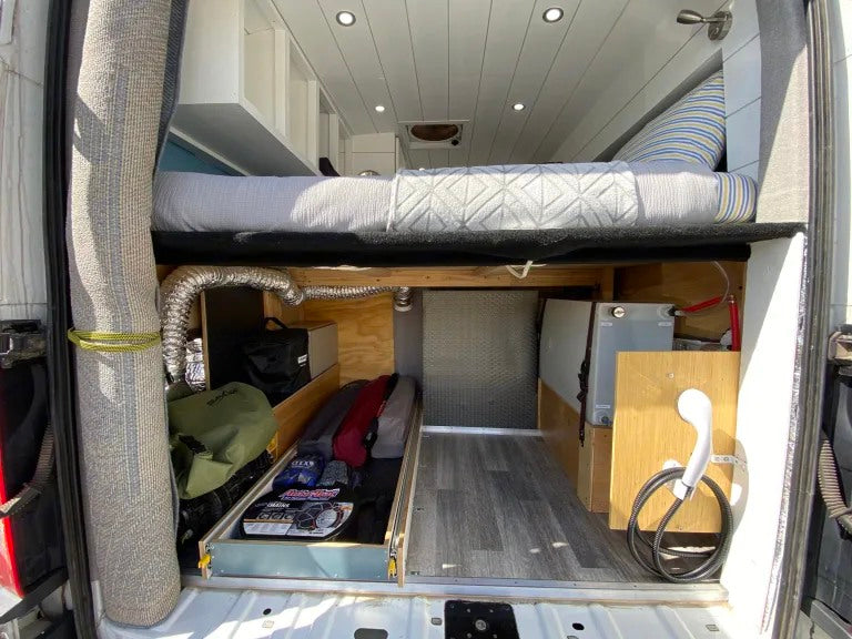 RV rental: Camper van's organized rear storage area. Raised bed above, utilities like a shower & water tank below. — photo 10