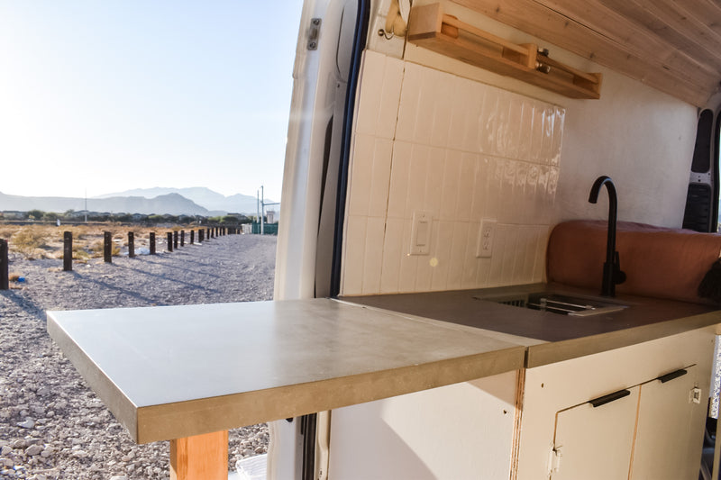 RV rental ready: Spacious camper van interior with a modern kitchenette, showcasing a concrete counter, sink, & mountain views. — photo 18