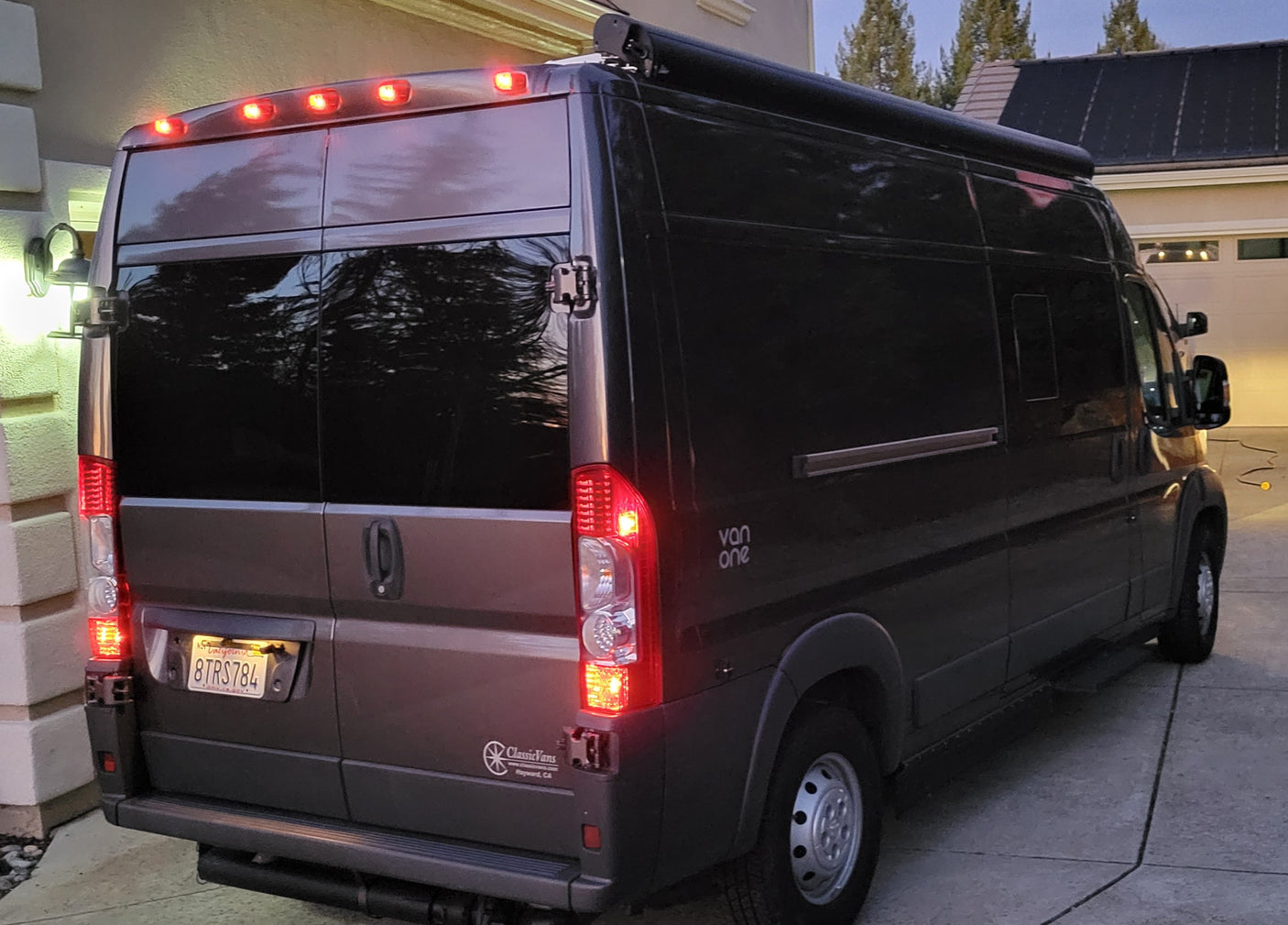 Dark gray camper van RV rental parked on a driveway with its rear lights on, ready for travel and adventure.