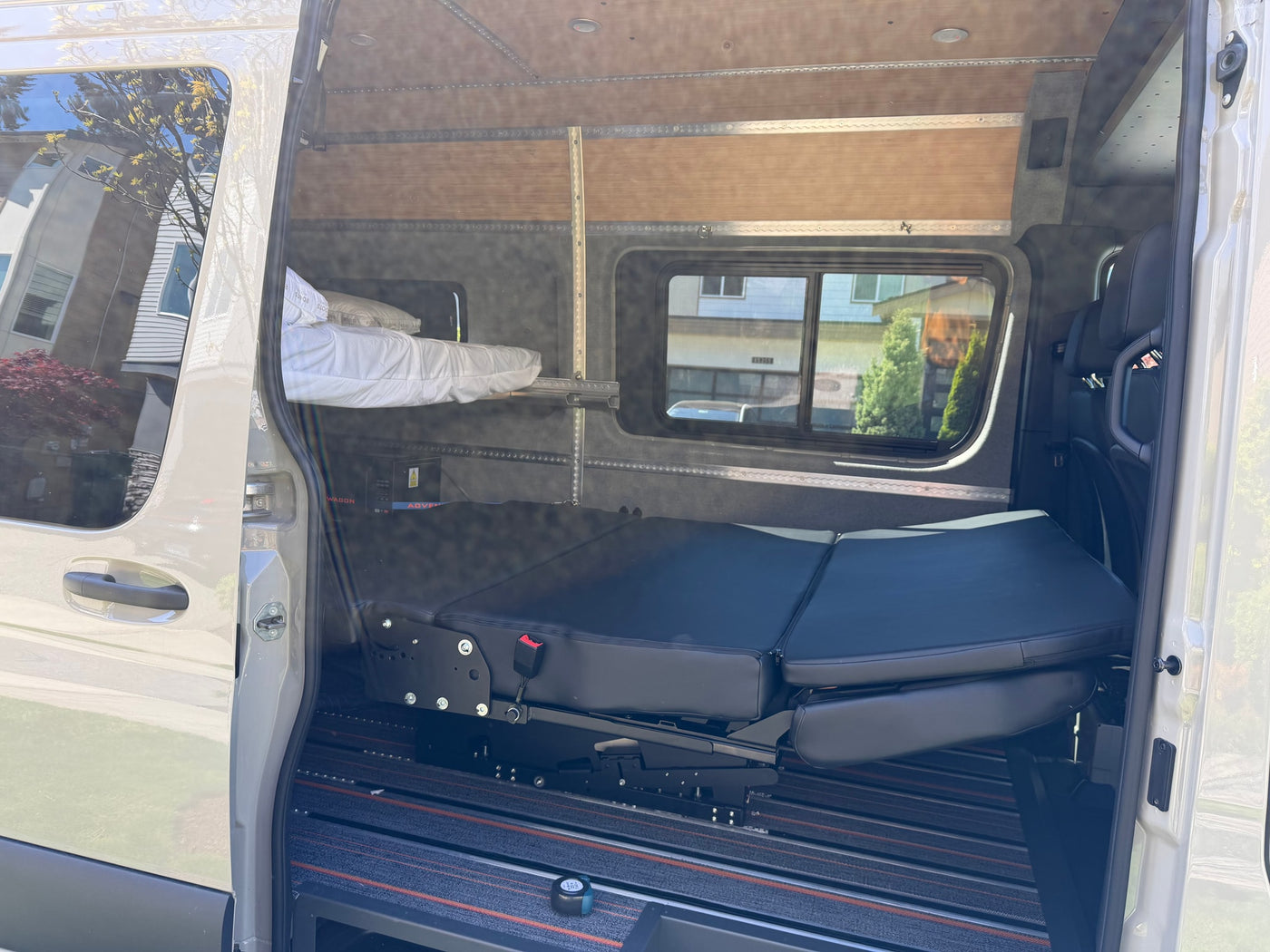 Open side door reveals a well-equipped rv rental interior with a foldable bench/bed, upper bunk, and modular track system for travel. — photo 8