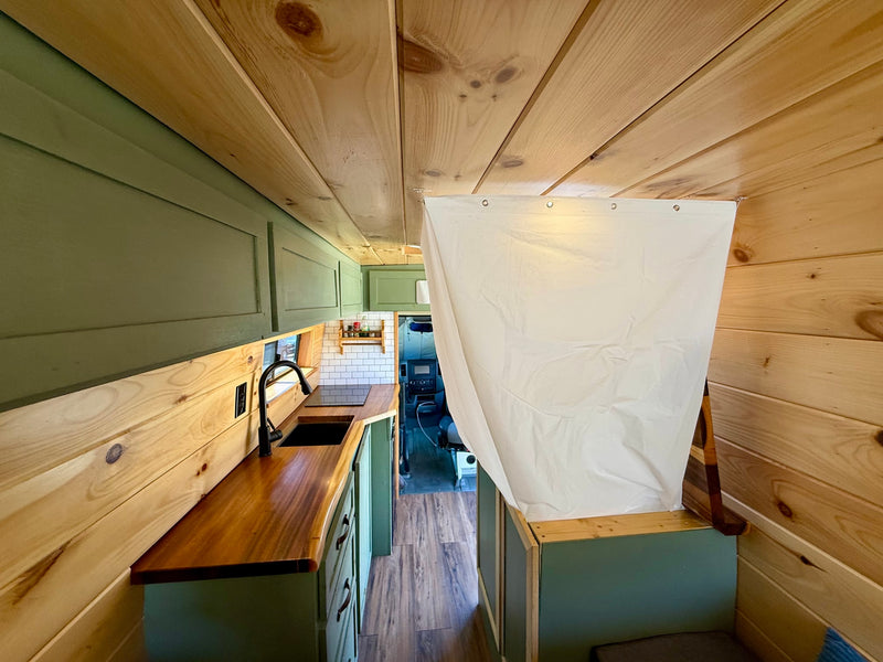 RV rental's inviting interior: modern kitchen with wood counters & green cabinets, leading to a curtained living space. — photo 18