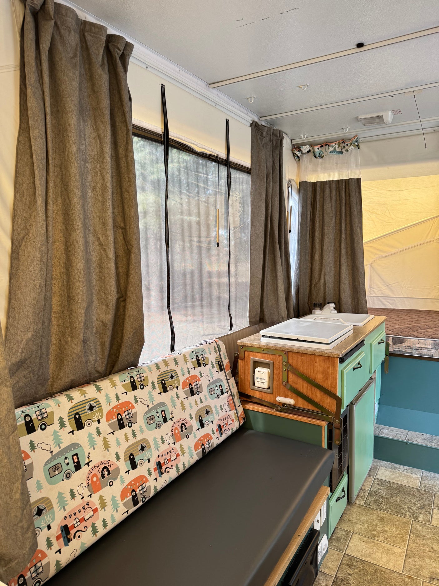 Cozy RV rental interior with a bench seat featuring camper-themed fabric, kitchenette, and curtains.