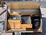 Open rear hatch of a Utah teardrop RV rental, showing its outdoor kitchen with sink, stove, and fridge.