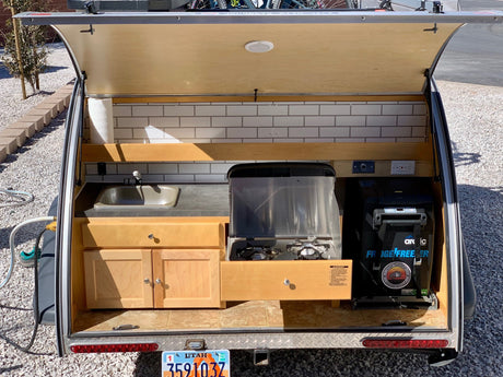 Open rear hatch of a Utah teardrop RV rental, showing its outdoor kitchen with sink, stove, and fridge.