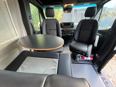 Interior of an RV rental featuring swivel seats, a dinette table, and safety equipment like a fire extinguisher.