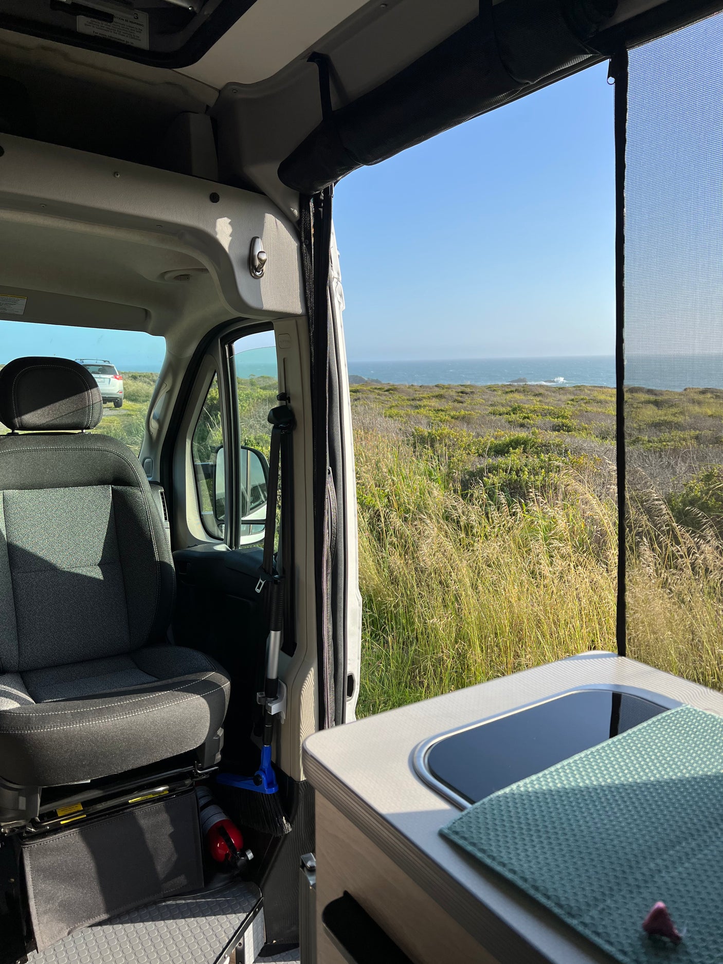 Coastal bliss from an rv rental: passenger seat, kitchen, and ocean views through a mesh screen.