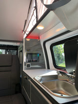 Experience an RV rental: Interior view shows a campervan kitchen with sink, counter, and integrated control panel. Ideal for travel.