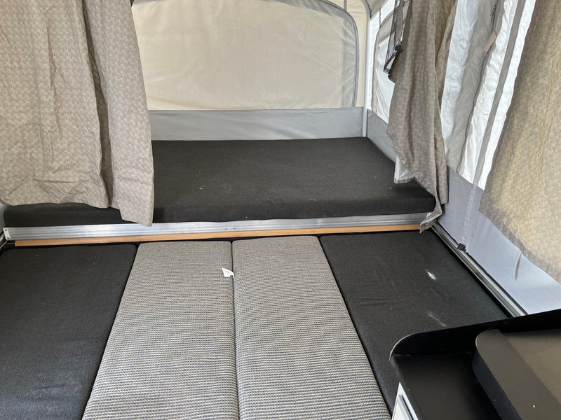 RV rental pop-up camper interior: raised sleeping area with dark grey mattress and floor cushions for comfort. — photo 7