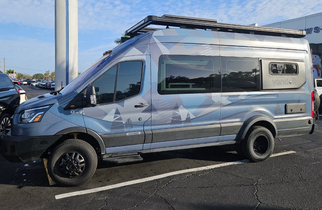 This custom-wrapped adventure camper van, featuring off-road tires and a roof rack, is ready for your next RV rental journey.