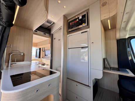 Explore this modern rv rental interior: kitchen with sink, induction hob, fridge, microwave, and handy laptop workstation.