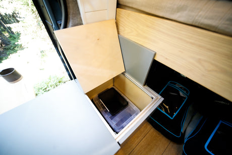 Discover smart storage in this RV rental! A lift-up wooden lid reveals a compartment with a clear bin & device.