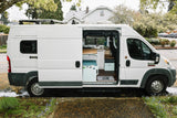 This white RV rental camper van shows its open side door, revealing a functional interior with kitchen & living space.