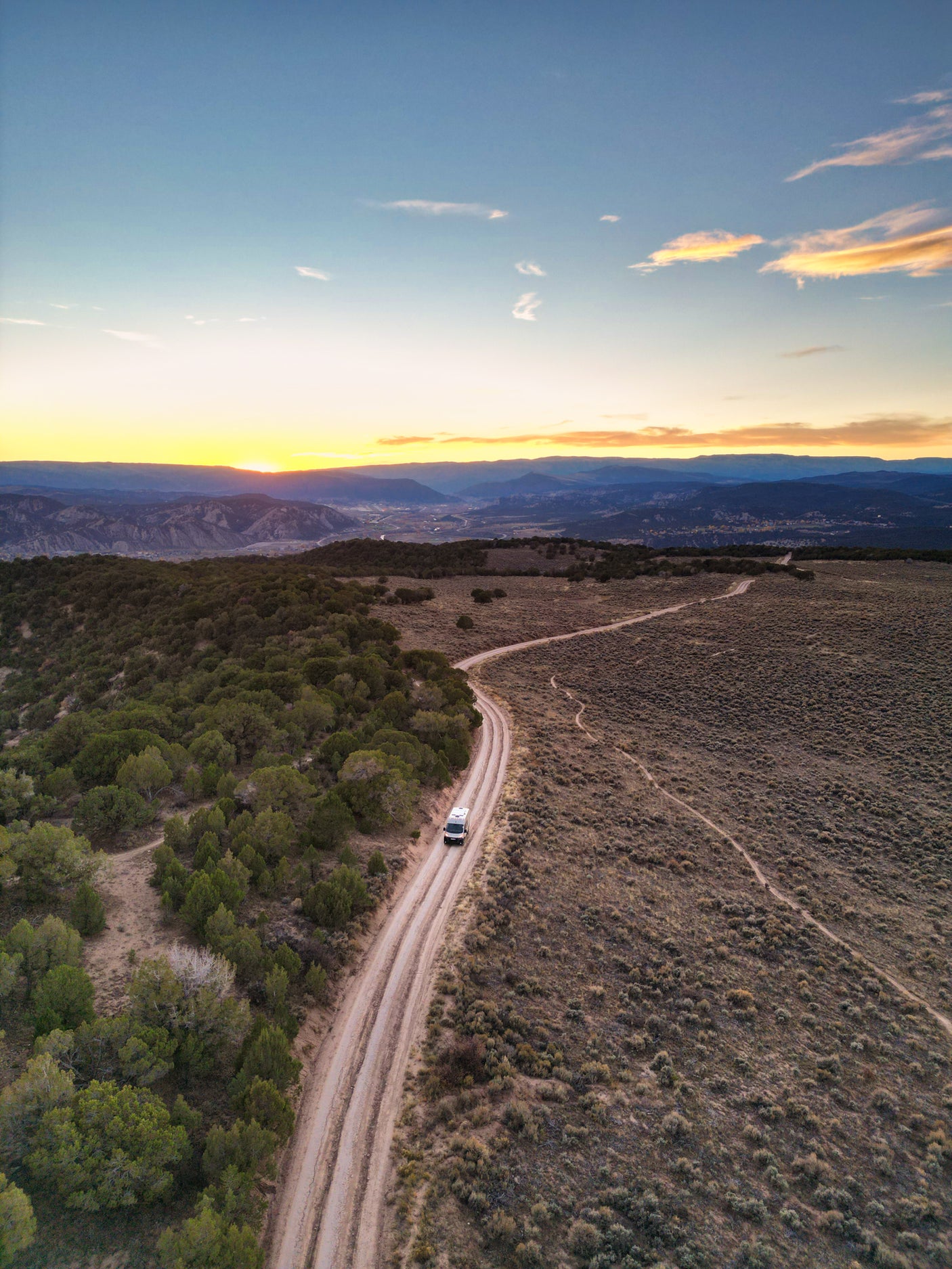 Experience an RV rental adventure! A white camper van travels a scenic dirt road through scrubland under a vibrant sunset.