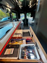 Organized **rv rental** interior with kitchen counter, open drawer showing batteries, remotes, and headlamps, plus seating.