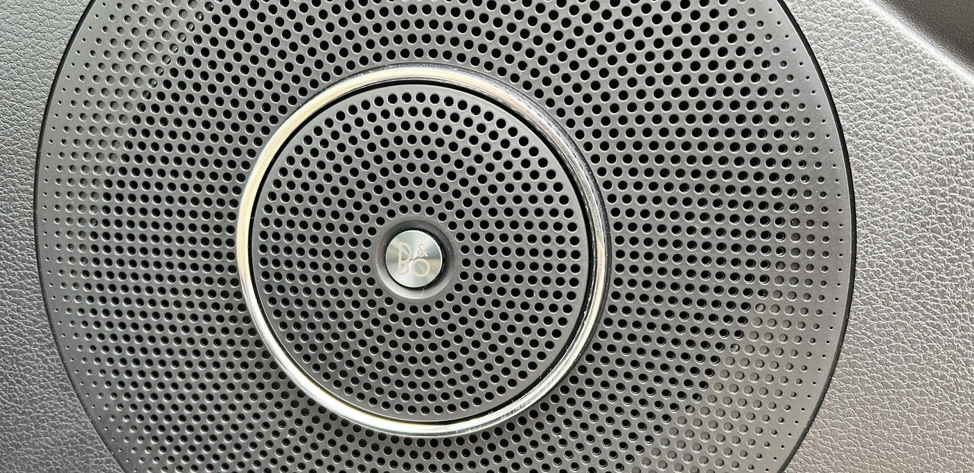 RV rental: High-fidelity B&O audio speaker grille, showing perforated pattern and chrome ring.