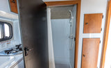 Inside an RV rental: a compact kitchen with stove and sink, and a bathroom door open to a small shower.