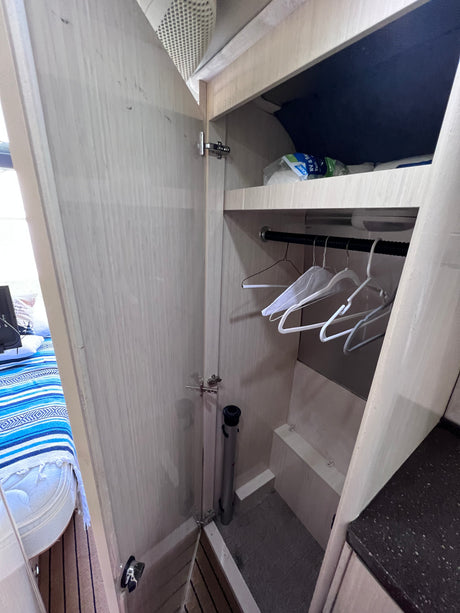 Compact RV rental wardrobe with hanging rod, white hangers, and upper shelf storage for travelers' gear.