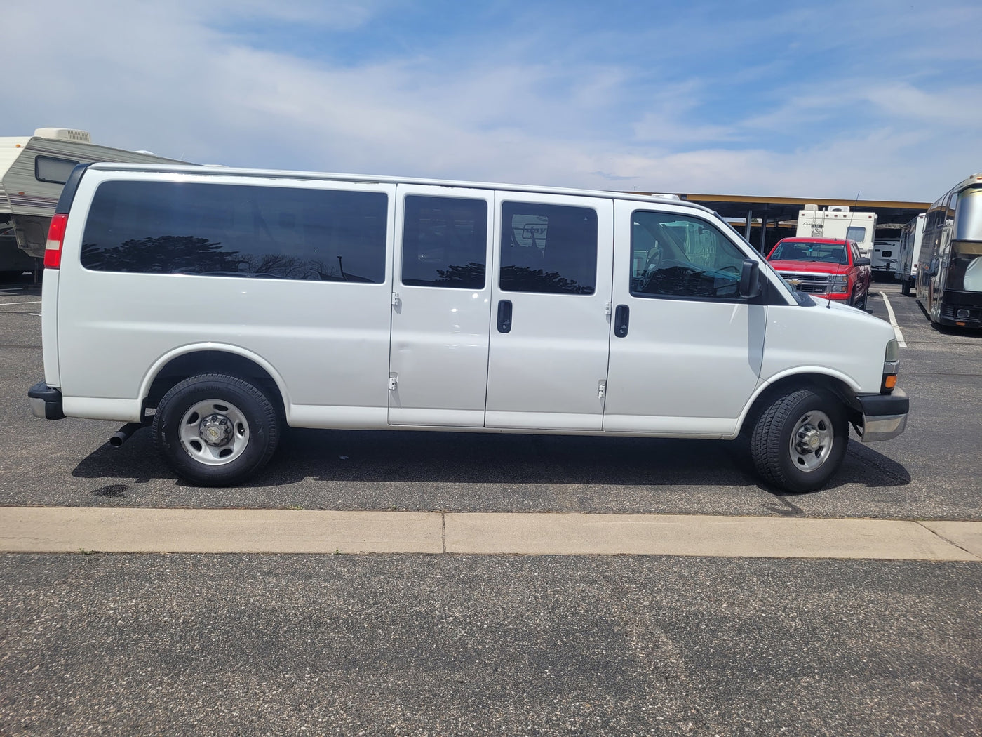 White extended van parked at an RV rental facility, surrounded by various RVs and a red truck under a blue sky. — photo 7