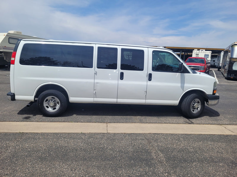 White extended van parked at an RV rental facility, surrounded by various RVs and a red truck under a blue sky. — photo 7
