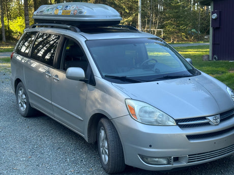 Silver minivan with roof box, ready for adventure like an rv rental, parked on gravel. Ideal for road trips & camping.
