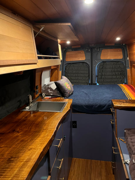 Interior of a beautifully crafted RV rental, showing a bed, integrated kitchen sink, and rich wooden finishes.
