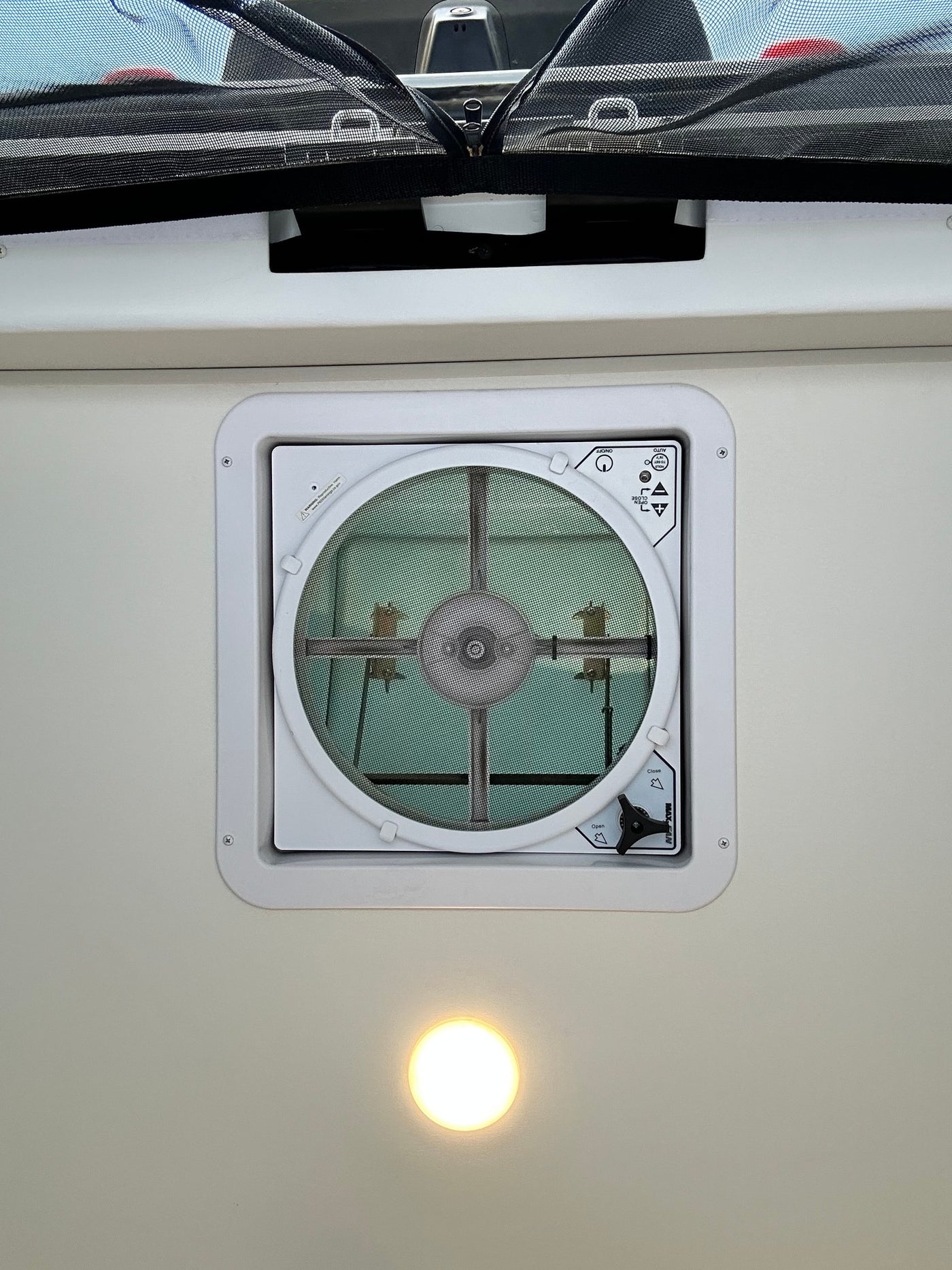 RV rental overhead view: MaxxAir ceiling vent fan with screen, an overhead light, and a black mesh privacy screen. — photo 4